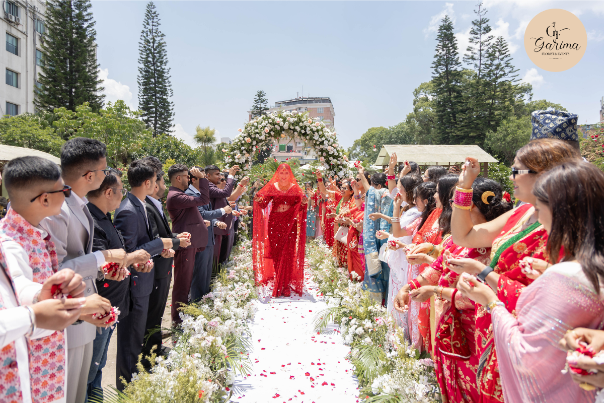 Nepali bride walking down a flower-lined wedding aisle surrounded by family and guests 