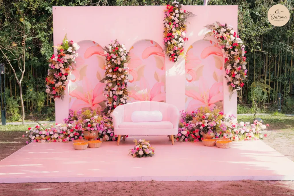 pink outdoor Haldi backdrop with floral arches and seating in natural daylight